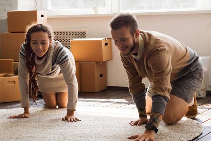 a young man and woman unroll a rug while unpacking boxes